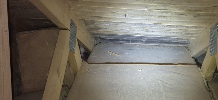 Vind med träbalkar och betongplattor, mörka fläckar som tyder på mögel och potentiellt läckage.