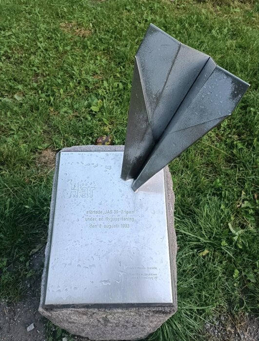 Skulptur av ett pappersflygplan i metall monterat på en sten med inskription om JAS 39 Gripen-kraschen 1993.