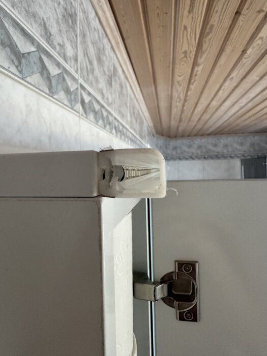 LED-list med små lampor sitter på kanten av en vit skåpdörr. Tak och vägg med klinker syns i bakgrunden.