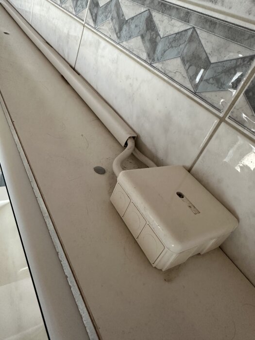 Bilden visar en LED-list och en kopplingsdosa på en bänkskiva i ett badrum med kakelvägg i bakgrunden.