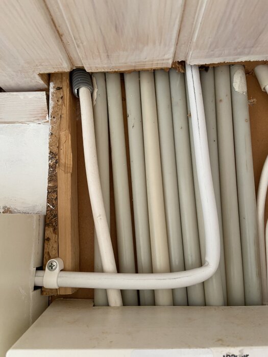 Kabeldragning med skarpa vinklar under träpanel, del av installation för laddbox, med flera vita kablar synliga.