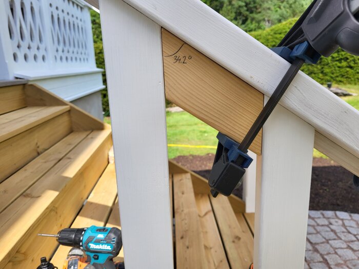 Trätrappa med monterade staketribbor. En borrmaskin ligger på ett trappsteg och en klämma håller en ribba på plats.