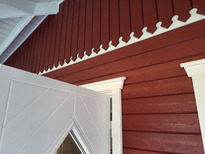 Röd träfasad med vitmålad snickarglädje och dörr.