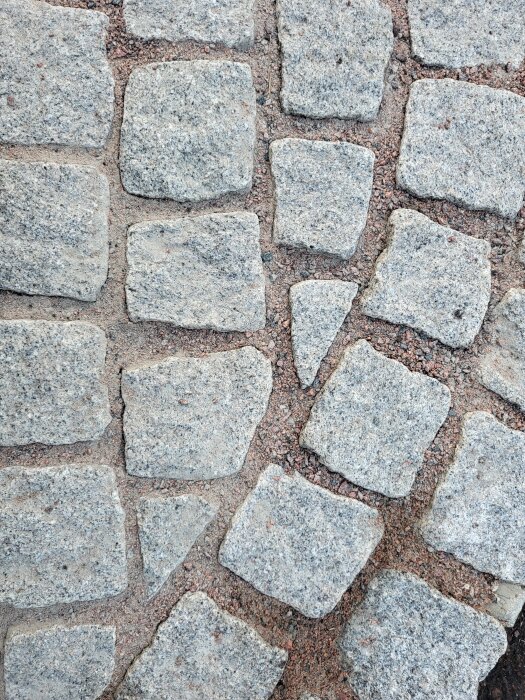 Kullerstenar lagda i ett mönster på en yta med synliga fogar av sand eller grus emellan.