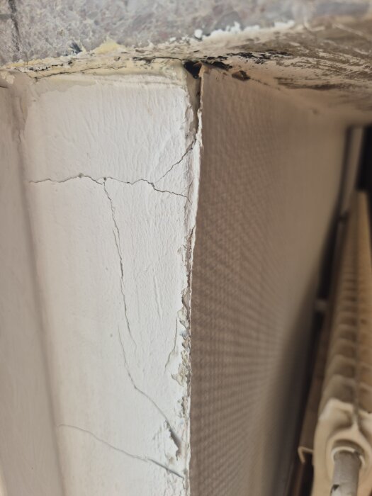 Vägg med spruckna ytor där gammal glasfiberväv böjer sig från underliggande tapet.