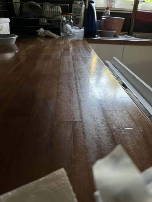 Träbänkskiva i kök med matt yta, omgiven av köksredskap och ett fönster i bakgrunden.