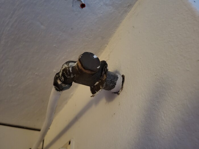 Rörförbindelse med en ventil och en koppling på en vit vägg, del av en inomhusinstallation.