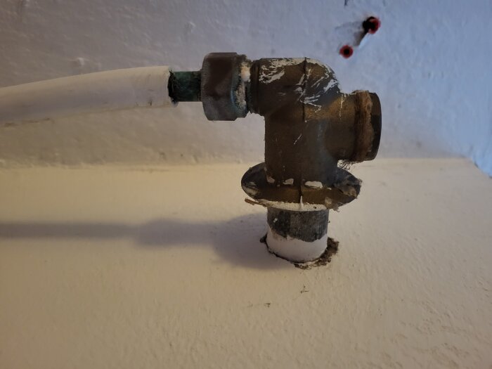 Ventilkoppling på insida av vitmålad vägg, ansluten till ett rör med vit tejp runt fogen.