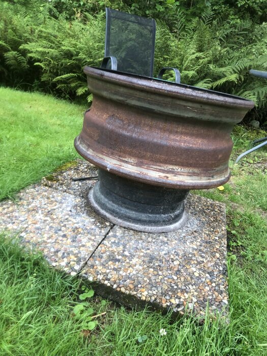 Eldplats med två bilfälgar staplade på trädgårdsplattor, omgiven av gräs och växter. En stol står i bakgrunden.