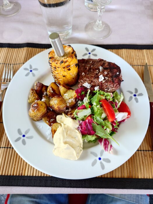 Tallrik med grillad rostas, rostad färskpotatis, majskolv, bearnaisesås och sallad med tomat.