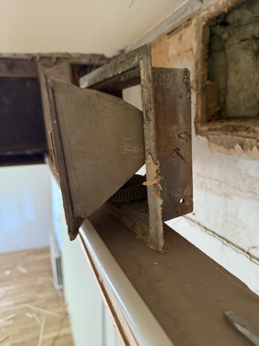 Gammal ventillucka i väggen av ett hus från 1928, delvis borttagen panel visar isolering och glipa som leder ut till utsidan.
