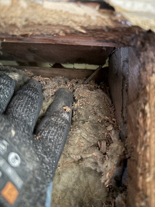 Gammal ventillucka i vägg med hål mot utsidan, utan diffusionsspärr och luftspalt, visad vid renovering av tak i äldre hus. Handske och isolering synliga.