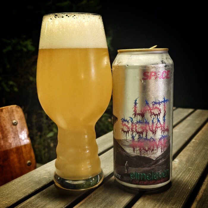 En ölburk märkt "elmeleven" bredvid ett glas fyllt med gyllene öl på ett träbord.