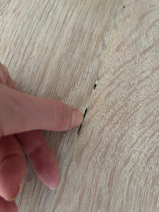 Finger pekar på en spricka mellan parkettbrädor på ett nyligen behandlat golv. Bristerna i fogningen syns tydligt.