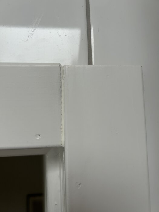 Målad dörrkarm med synliga sågmärken och blottat trä vid övergången mot taket.