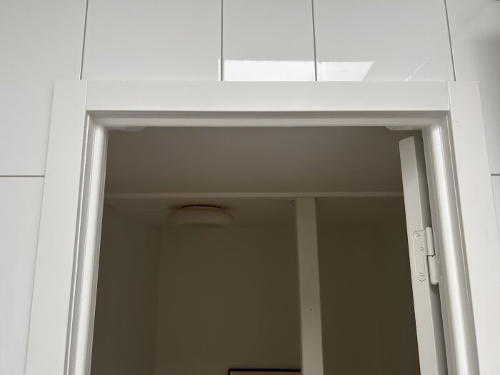 Vit dörrkarm i badrum med synligt trä och ojämna snitt. Tecken på avsågning syns tydligt på närbilden av karmens övre del.