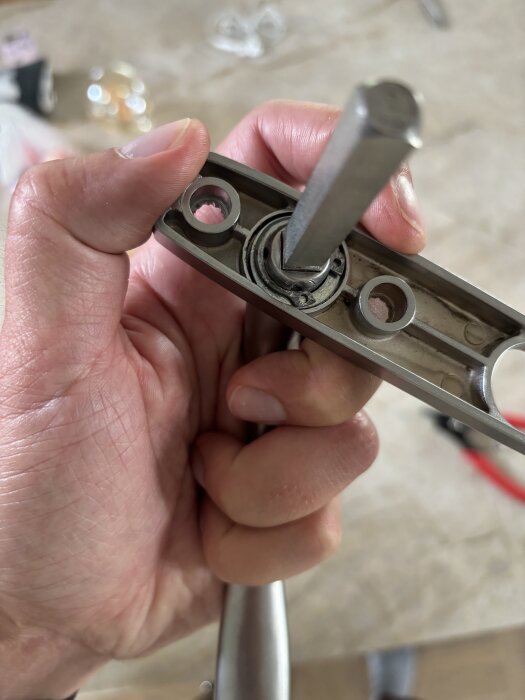 Närbild på en hand som håller ett dörrhandtag med en monterad sprint, synlig metallmekanik och hål för skruvar.