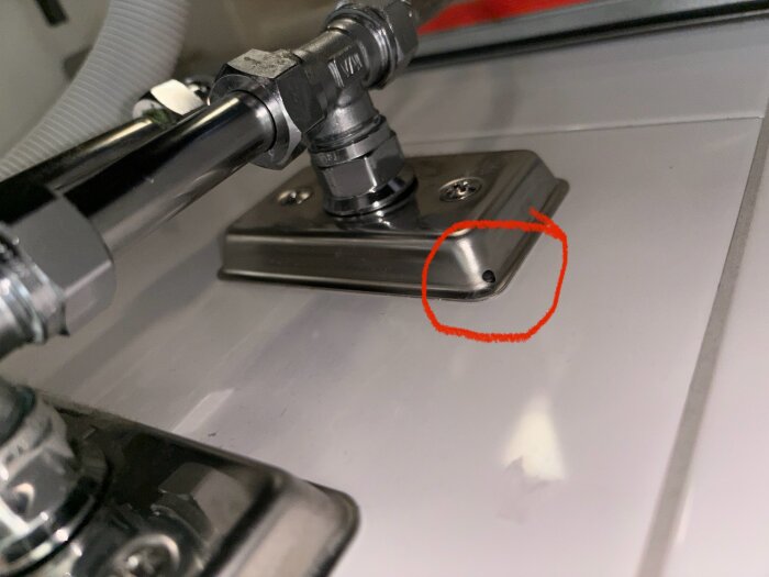 Läckage under badrumssänk där rör ansluter till väggen, markerat med röd cirkel i närbild.