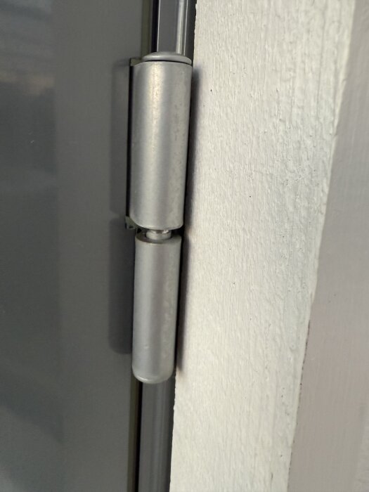 Dörrgångjärn justerat med insex för att fixa glapp, syns på en närbild av dörrkarmen.