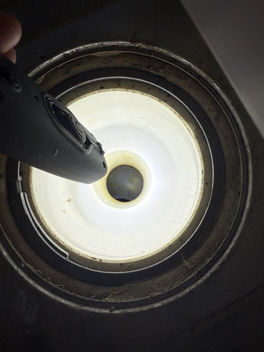Duschens avlopp utan vattenlås där rör och golvbrunn syns. Hålla en lampa ovanför för att lysa in i avloppet, smuts synlig runt kanterna.