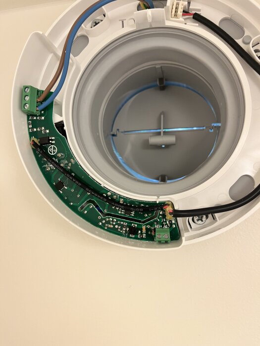 Öppen takenhet med elektronik och kablar, monterad på vit bakgrund.