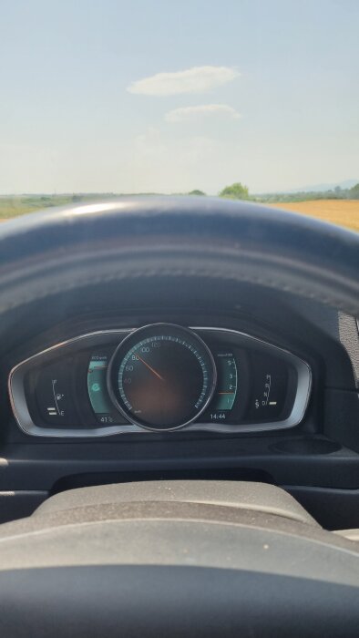 Bilens hastighetsmätare visar 80 km/h, ratt sedd i förgrunden och suddig utsikt av landskapet genom vindrutan i bakgrunden.