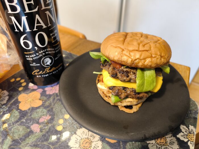 Hemlagad högrevsburgare med ost, dressing, ketchup och sallad på ett fat bredvid en flaska öl.