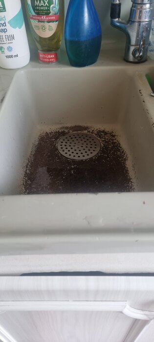 Sliten diskho av emaljbeklädd glasfiber med synliga fläckar, omgiven av diskmedelsflaskor och en kran, i behov av byte.