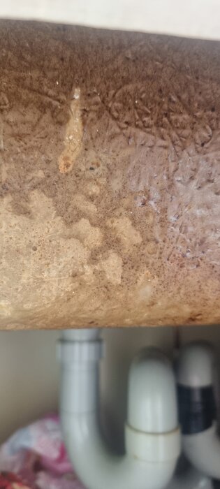 Närbild av undersidan av en gammal, sliten diskbänk i emaljbeklädd glasfiber med synliga rörkopplingar.