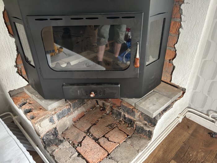 Svart eldstad installerad i hörna med synliga tegelstenar och rör.