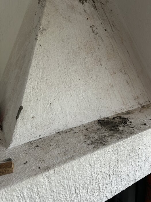 Vit murad yta på öppen spis, delvis sotad och sliten, med texturfråga.