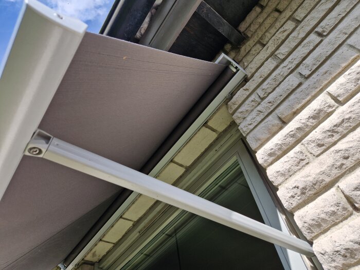 Markis monterad på vit tegelvägg över ett fönster, sedd från undersidan.