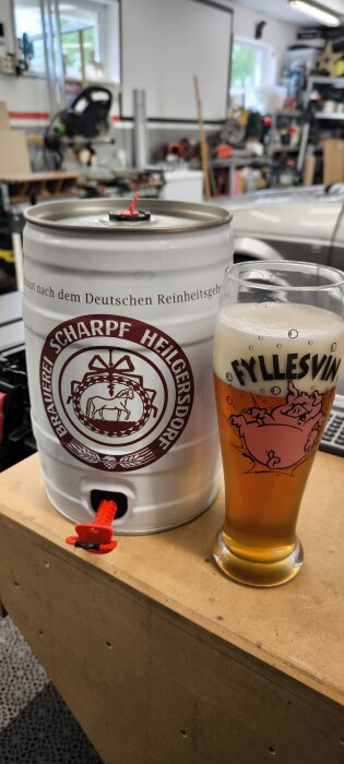 Öltunna och glas med gyllene öl, märkt med "Fyllesvin", i ett garage eller verkstadsmiljö.
