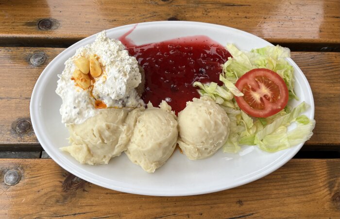 Tallrik med potatismos, lingonsylt, en klick sås, sallad med tomatskiva. Ligga på ett träbord.