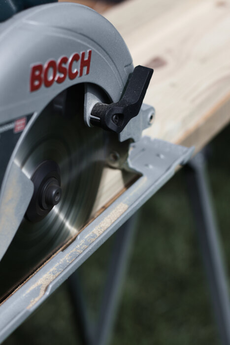 Cirkelsåg av märket Bosch som är i färd med att såga igenom en träskiva uppställd på ett arbetsbord.