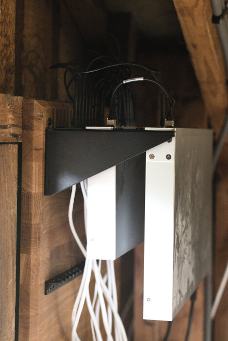 Svart och vitt serverrack med sladdar monterat på ekskiva i ett träförråd.