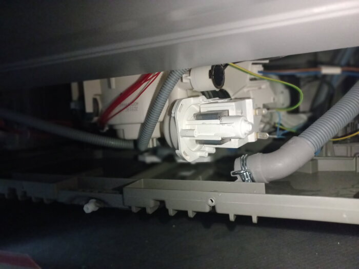 Interiör av en diskmaskin med synliga kablar och rör. Möjligen visar bilden pumpen som kan vara blockerad eller slangen för avfallsvatten.