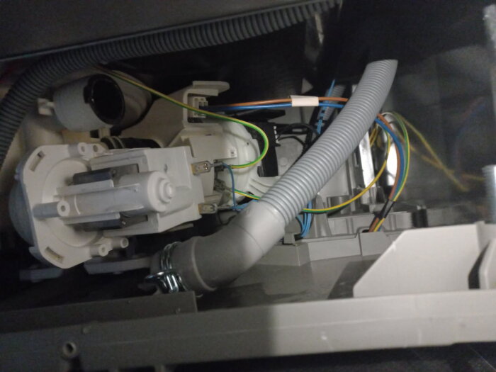 Diskmaskinens inre med synliga slangar, kablar och pumphus, potentiellt problem med restaurering av avfallstömning.