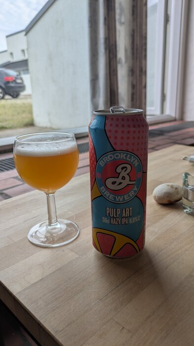 En burk Brooklyn Brewery Pulp Art IPA och ett glas öl på ett bord vid ett fönster.