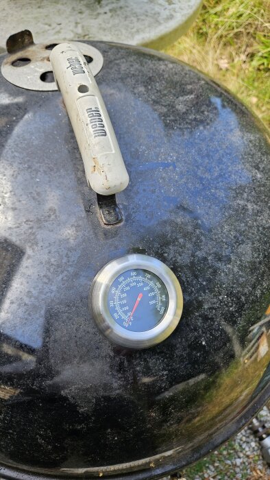 Grill med en nyinstallerad termometer på locket, bredvid ett Weber-handtag.
