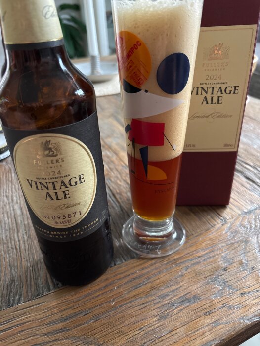 Flaska och glas av Fuller's Vintage Ale 2024 på ett träbord, med skum i glaset och förpackningen i bakgrunden.
