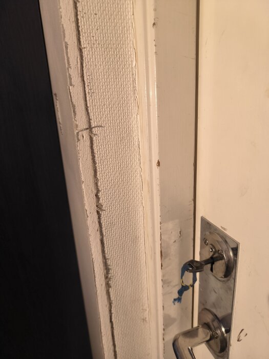Sliten dörrkarm och nylagd tapet vid en dörr med ett lås och handtag; nyckelhål har en blå lösningstejp på nyckeln.