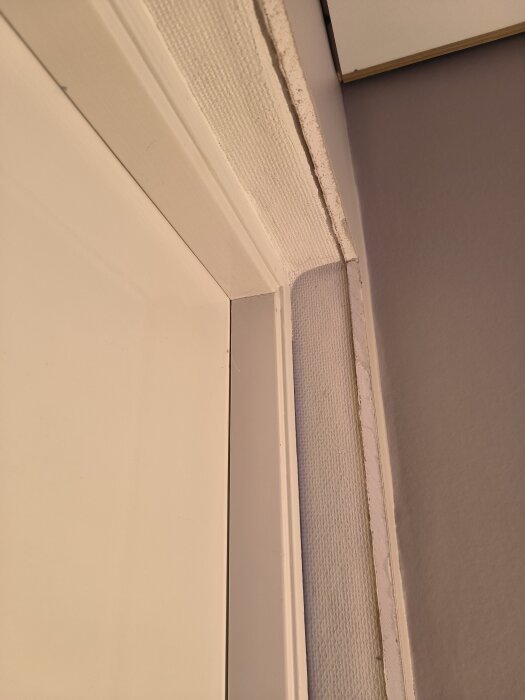 Dörrkarm med synligt gap mellan tapet och vägg, del av renoveringsprojekt där dörren ska fräschas upp med lack eller färg.
