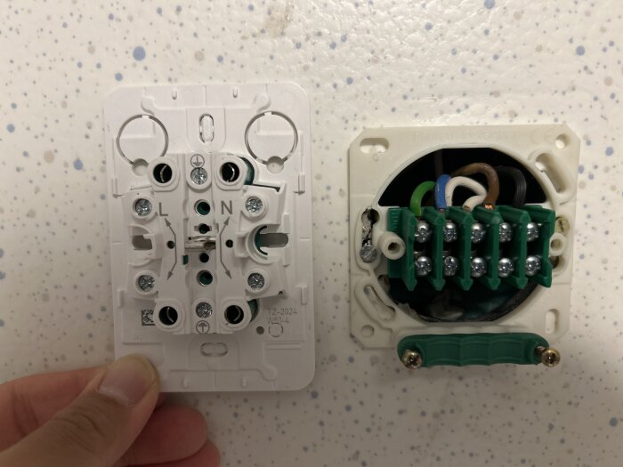 Bild av en väggmonterad kopplingsbox med blottade kablar och en vit plastpanel, redo för installation av ett vägguttag.