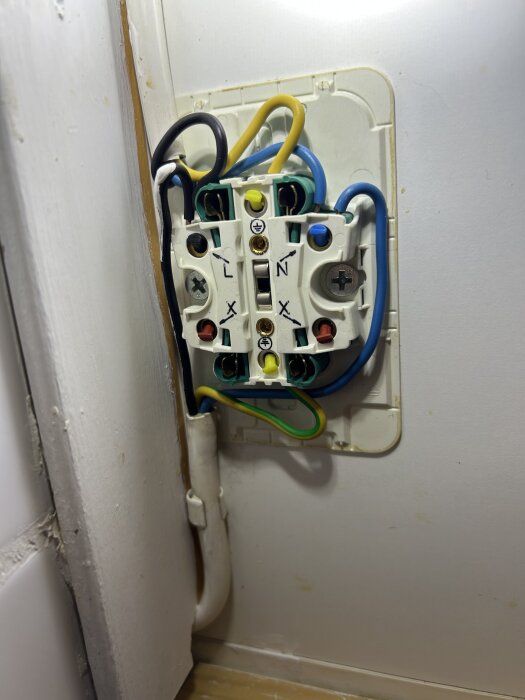 Öppet 2-vägs eluttag under köksskåp med synlig exponerad svart fasledare, flera anslutna kablar i olika färger, utan isoleringstejp.