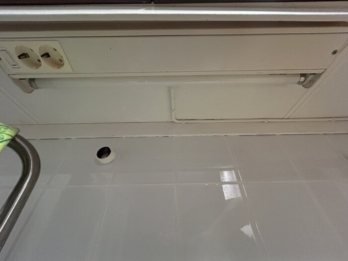 Gammalt tvåvägsuttag under köksskåp; synlig svart fasledare utan isolering, med lysrörsbelysning ansluten i fast installation.