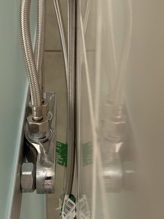 Baksidan av en duschkabin med två flexibla metallslangar och synliga rördelar. Rören sticker inte ut tillräckligt för montering.
