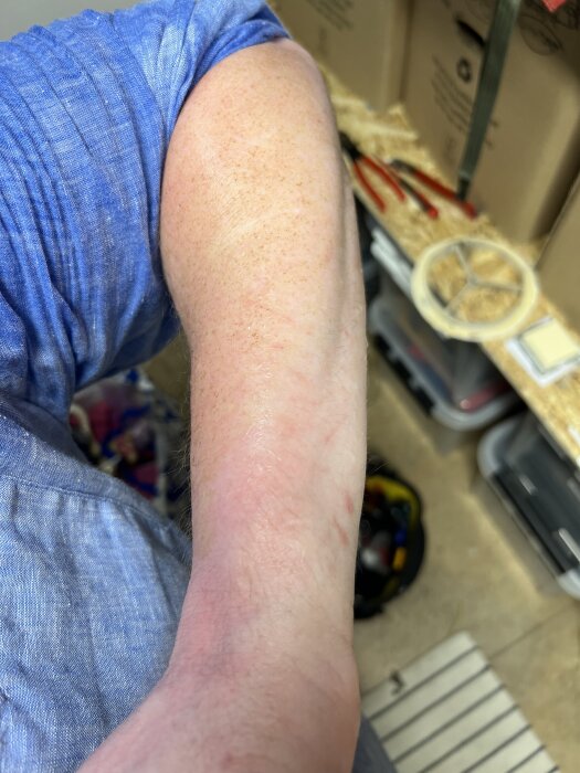 Person i blå skjorta med rödaktig arm i förråd, verktyg och kartonger i bakgrunden.