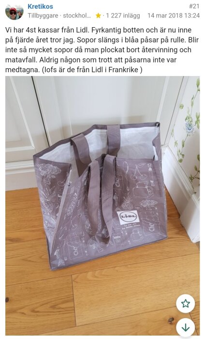 Brun Lidl-kasse med vita illustrationer av matvaror, stående på ett trägolv nära en vit vägg. Kassen har rejäla handtag.
