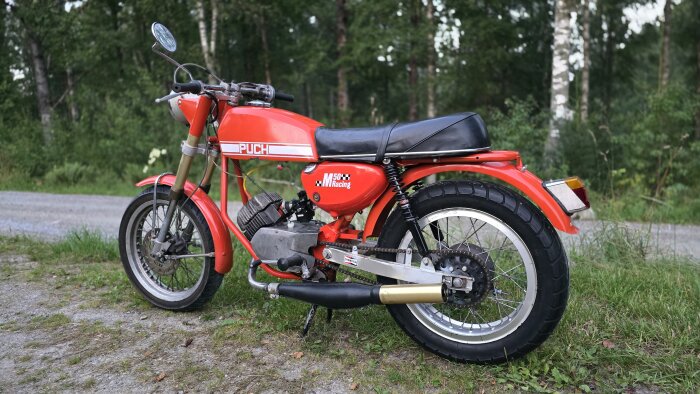 Röd Puch moped parkerad på en grusväg med skog i bakgrunden.